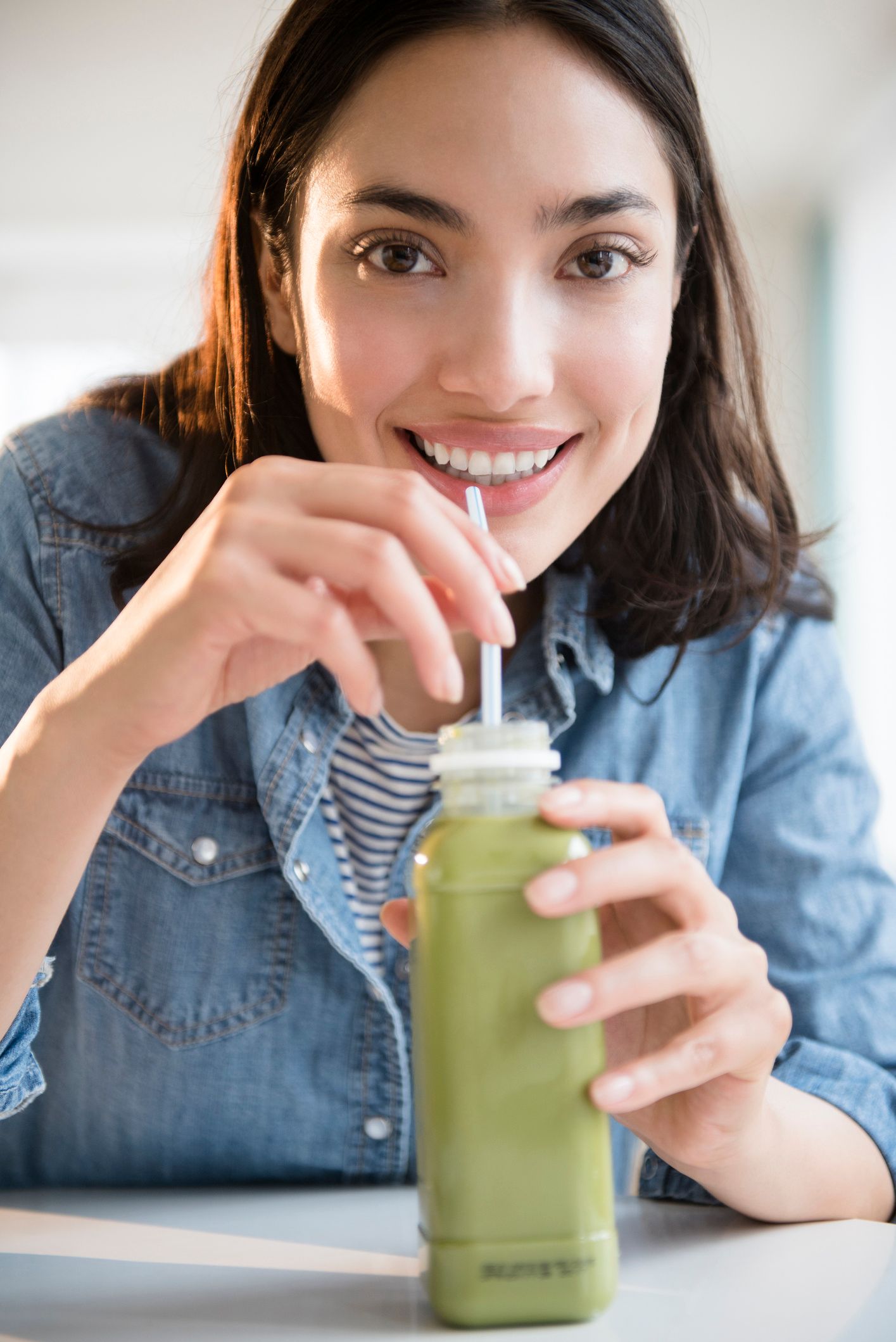 Brown-haired girl sips green liquid in a bottle